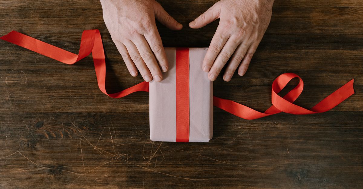 Top view of hands wrapping a gift with red ribbon on a wooden surface