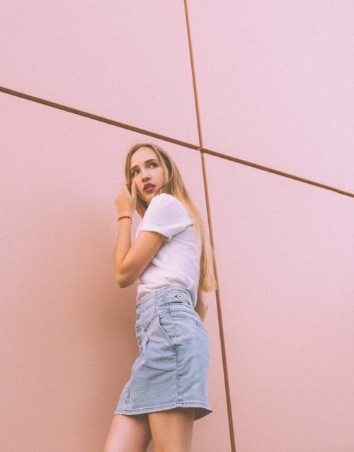 Confident young blonde woman standing near pink building and looking away