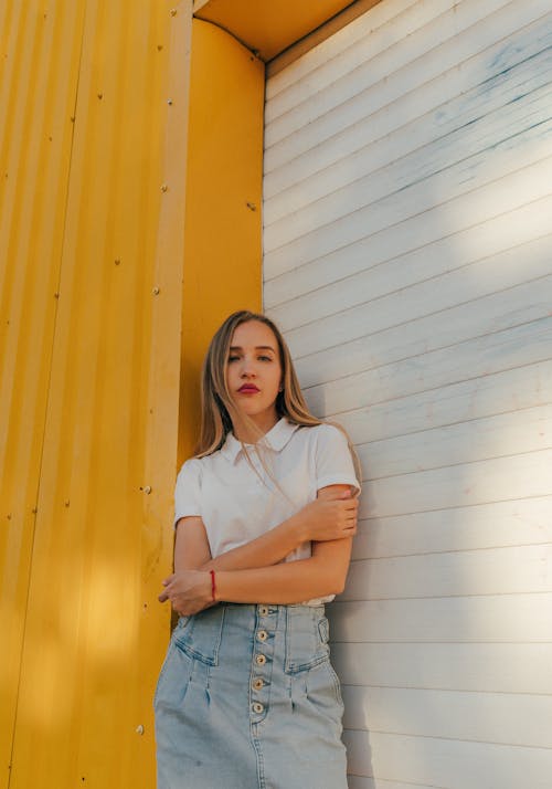 Serious young female millennial with long blond hair in stylish outfit looking at camera while standing near steel roller shutter door with crossed arms