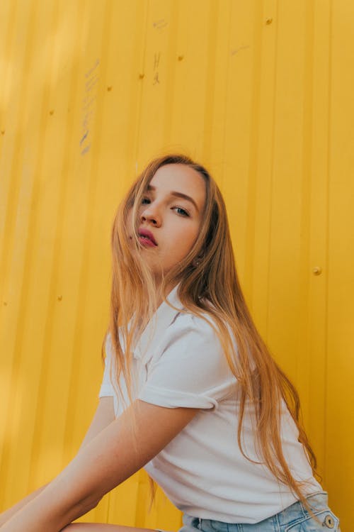 Cool young stylish lady sitting near yellow metal wall and looking at camera