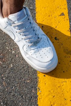 Close-up of a white sneaker stepping on a yellow line on an asphalt road.