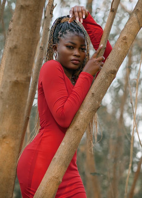 Young black woman standing near tree in park and looking at camera