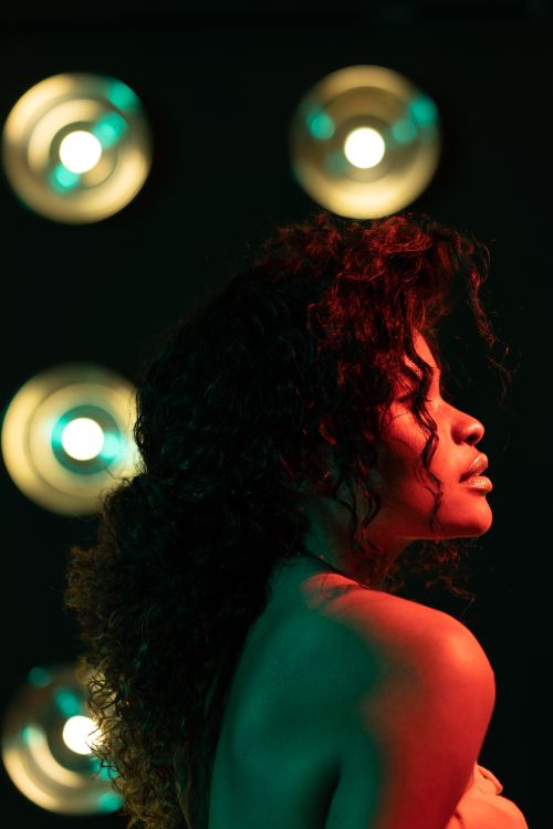 Free Side view portrait of a woman with curly hair in artistic lighting setup, evoking drama and elegance. Stock Photo