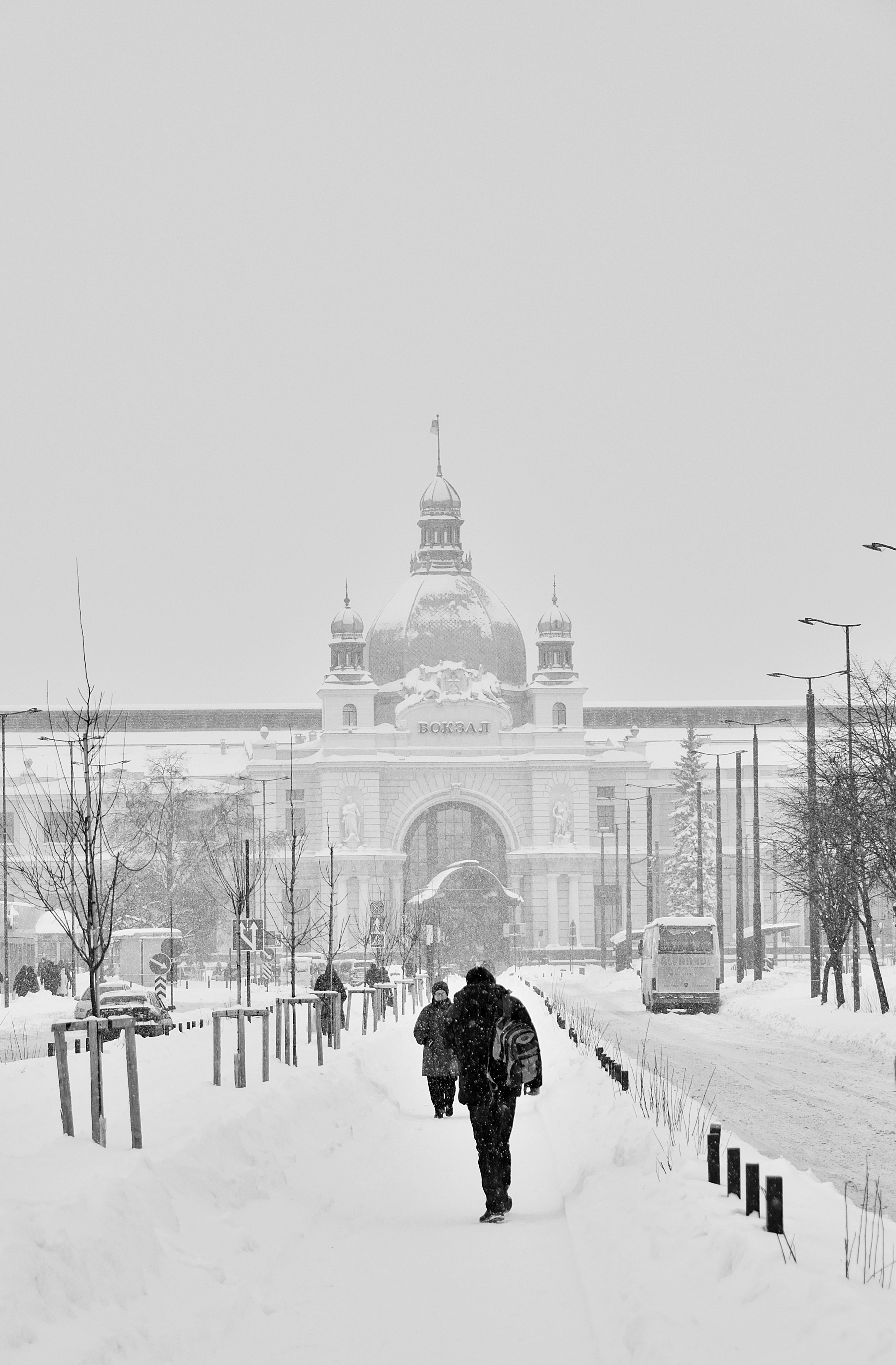 Lviv Railway Station captured during a snowstorm with people walking on a snow-covered street.