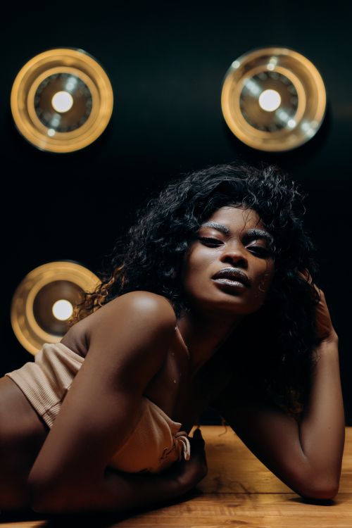 Free Elegant portrait of a stylish black woman posing with dramatic lighting on a wooden surface. Stock Photo