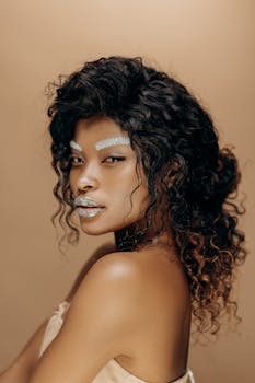 Elegant portrait of a woman with striking glitter makeup and curly hair in a professional studio setting.