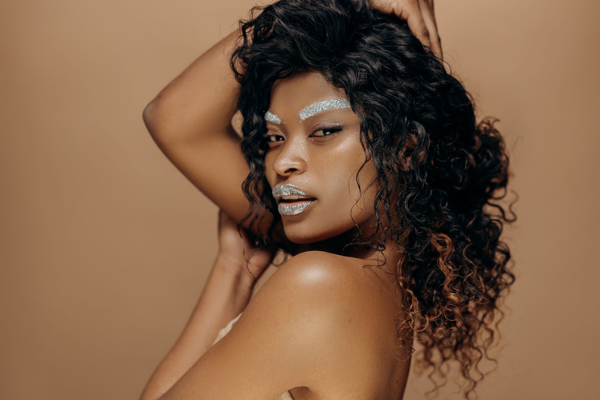 Portrait of a stunning model with glitter makeup, posing confidently in a studio setting.