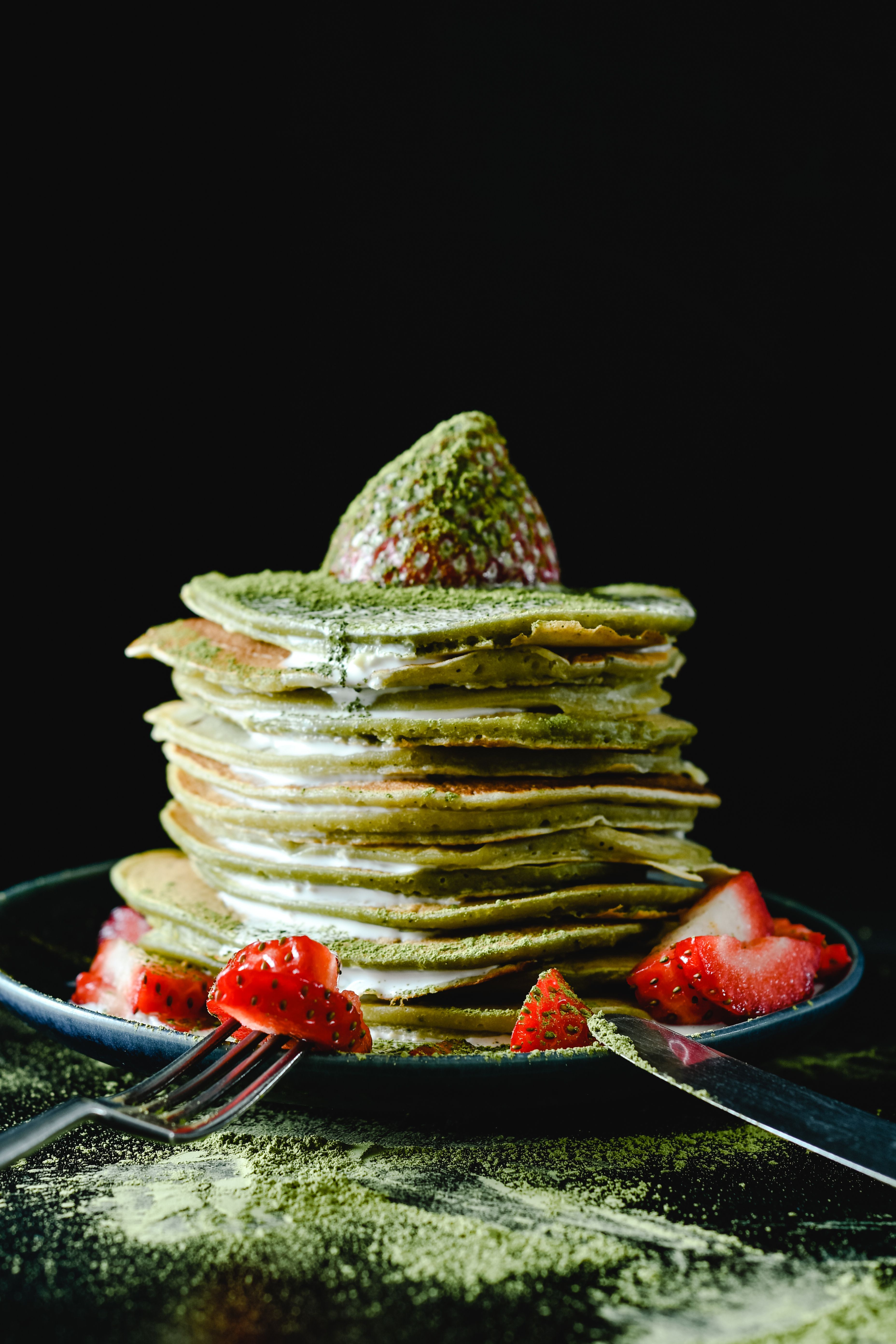 A mouthwatering stack of homemade matcha pancakes with fresh strawberries on a dark background.