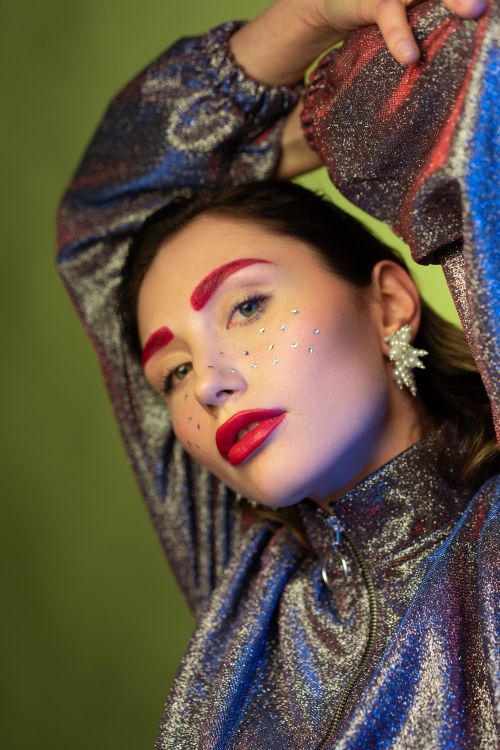 Free Close-up portrait of a woman in glittery attire with bold red makeup against a green backdrop. Stock Photo