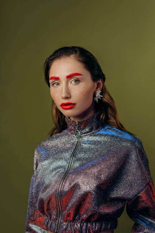 Free Stunning portrait of a woman in a glittery jacket with bold makeup against an olive background. Stock Photo