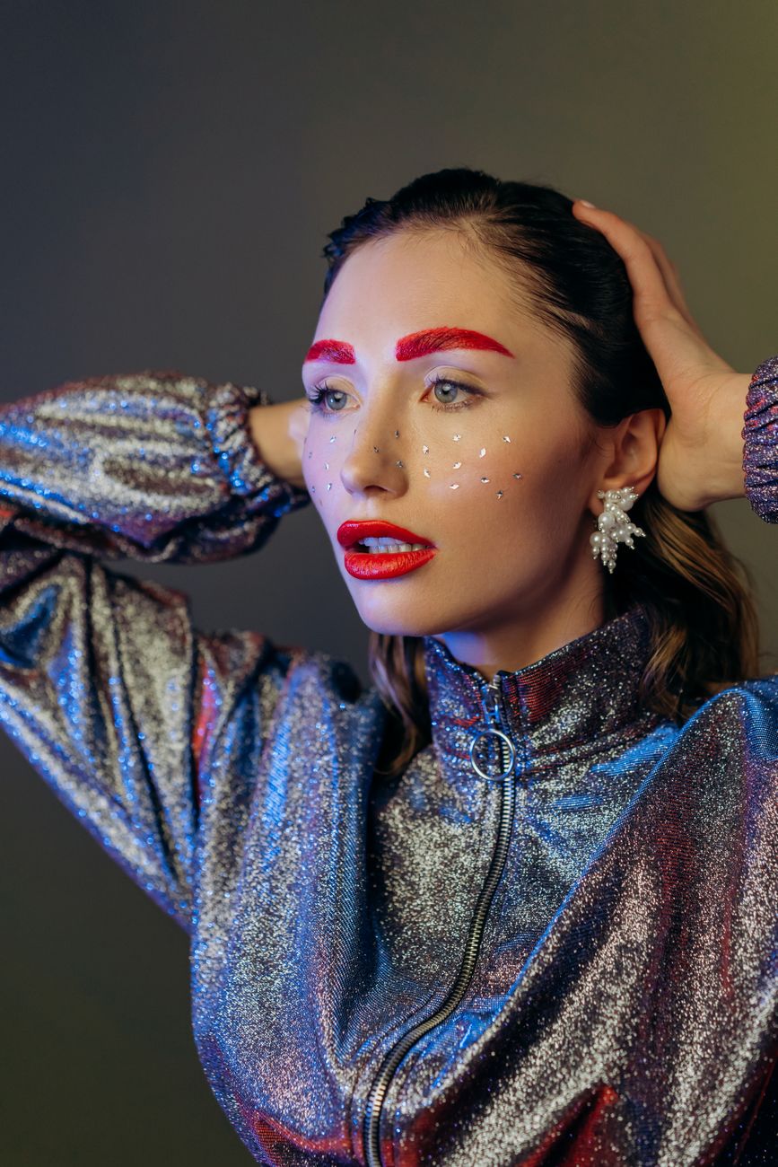 Close-up portrait of a woman with bold makeup, glitter, and a shiny outfit.