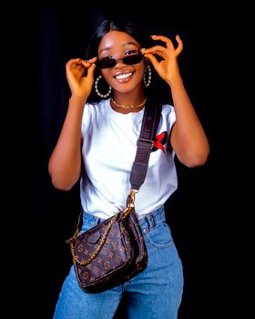 Fashionable woman in jeans and T-shirt smiling and posing with sunglasses and designer bag.