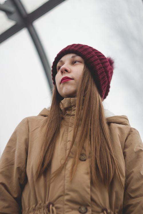 Free Portrait of a woman outdoors in winter attire, wearing a brown coat and red beanie. Stock Photo