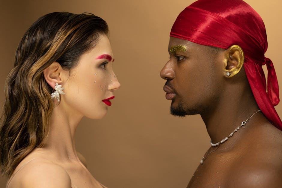 Artistic portrait of a man and woman facing each other with bold makeup and red hues.