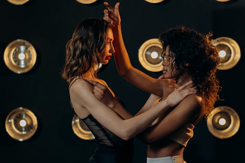 Two women posing dramatically with studio lights in the background, showcasing modern fashion style.