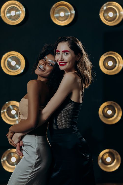 Free Two stylish young women smiling brightly in front of studio lights, embodying fun and fashion. Stock Photo