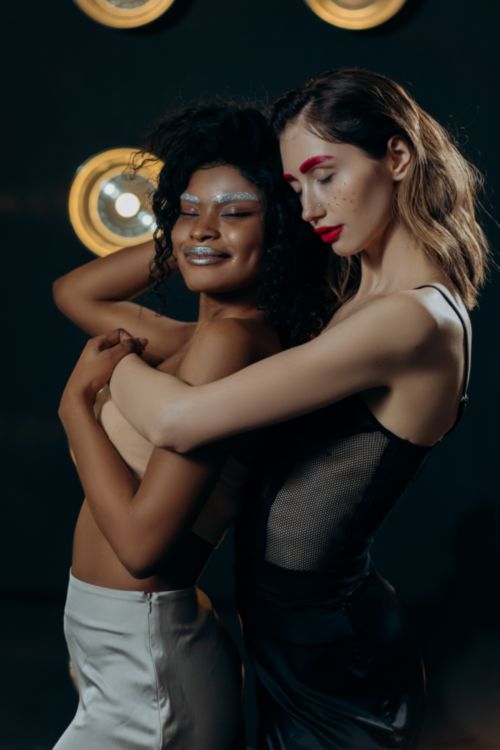 Free Two stylish women embracing with bold makeup in a studio setting, showcasing elegant fashion with dramatic lighting. Stock Photo