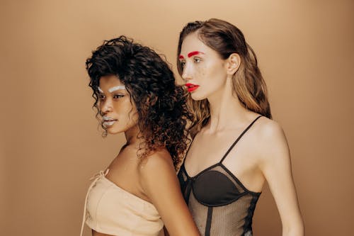 Artistic fashion portrait of two women with striking makeup and vibrant attire, showcasing creativity and style.