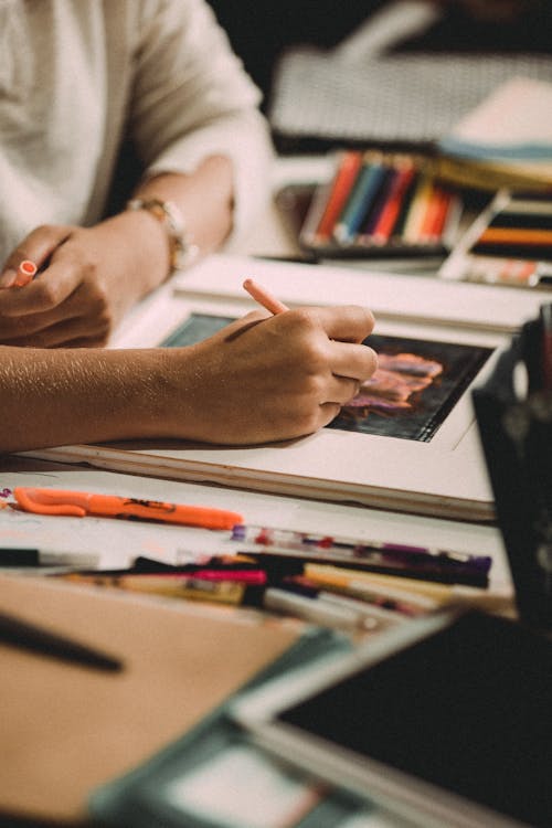 Crop anonymous female drawing picture at table with professional art tools in workshop