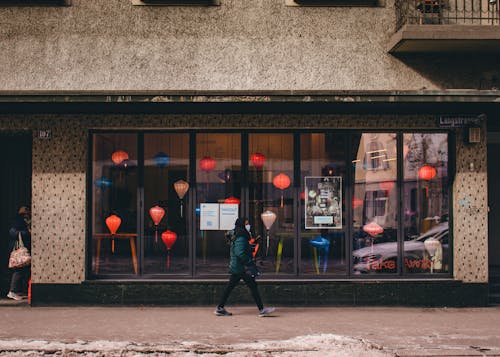 Person in Winter Clothing Wearing a Facemask Walking on the Sidewalk