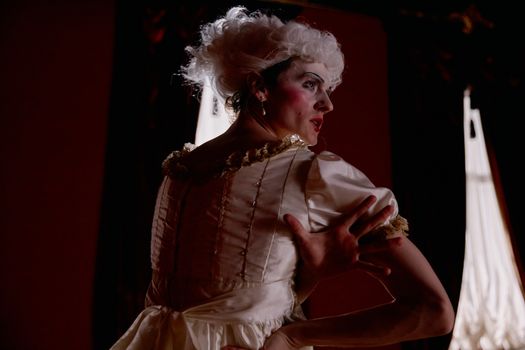 A theatrical performer in a historical costume striking an expressive pose indoors.