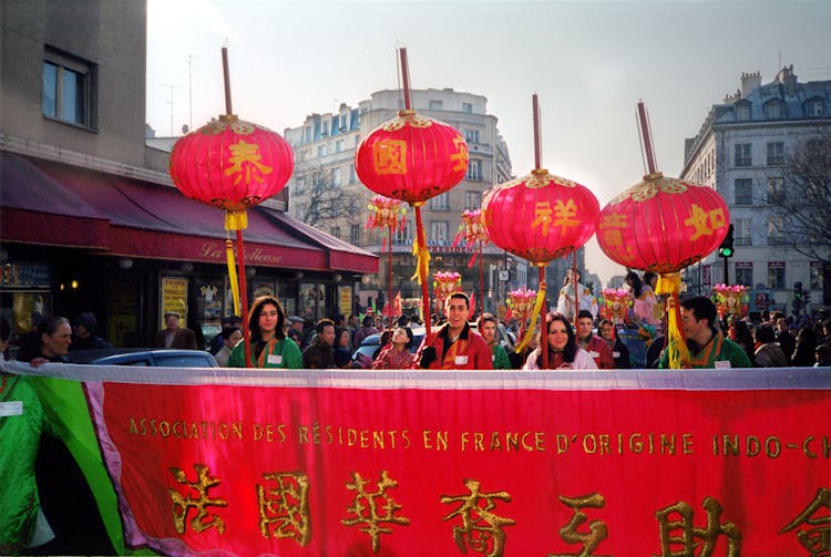 A Group Of People Holding Sticks With Red Chinese Lanterns During A Parade