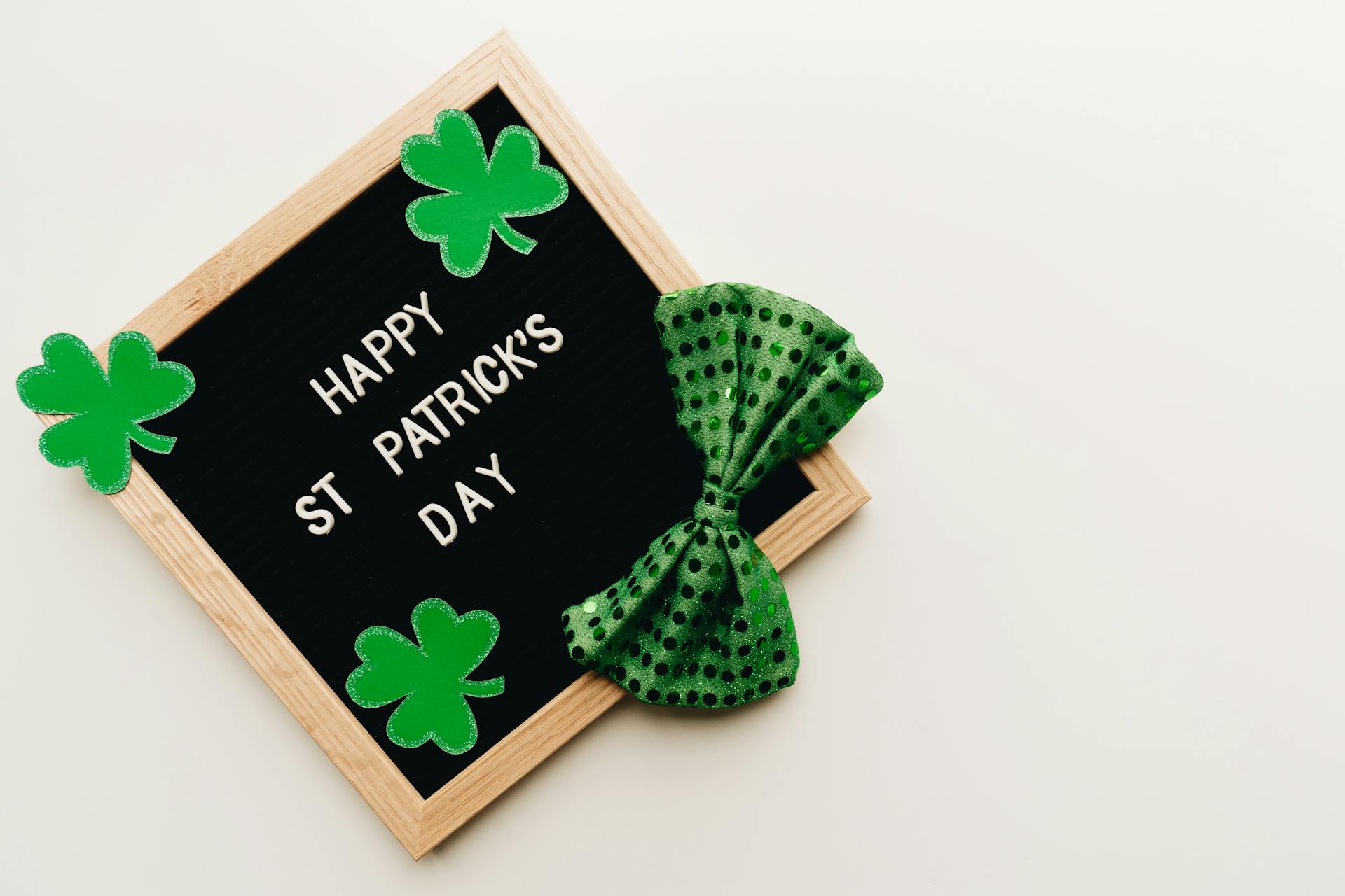 Celebratory St. Patrick's Day letterboard with green clovers and a polka dot bow tie on a white background.