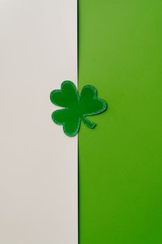Vertical shot of a green paper clover on a white and green background, symbolizing luck and St. Patrick's Day.