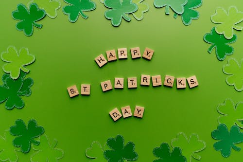 Scrabble Letter Tiles Saying Happy St. Patricks Day and Green Paper Clovers Scattered Around It 