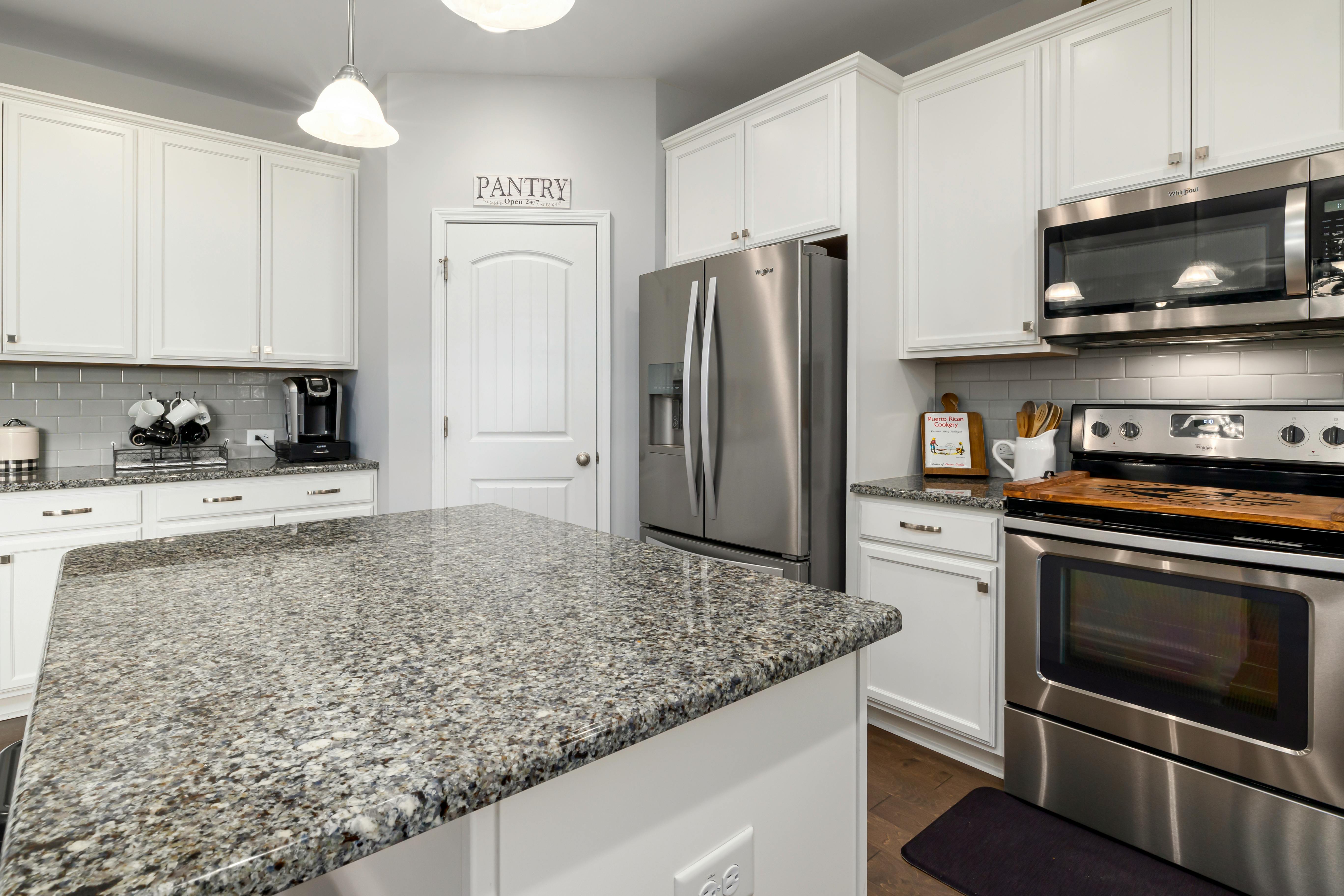 A contemporary kitchen featuring granite countertops, stainless steel appliances, and white cabinets.