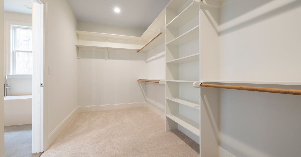A bright and spacious empty walk-in closet with white shelving and hanging rods, ideal for organizing.