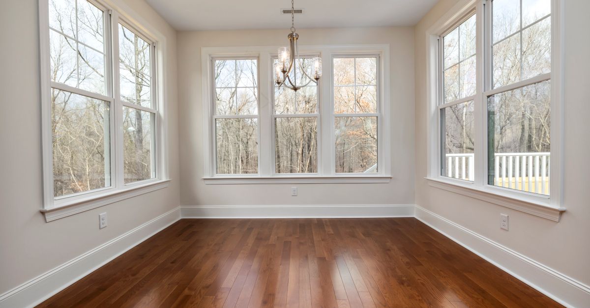 Spacious, empty room with large windows, wooden floor, and elegant chandelier, perfect for interior inspiration.