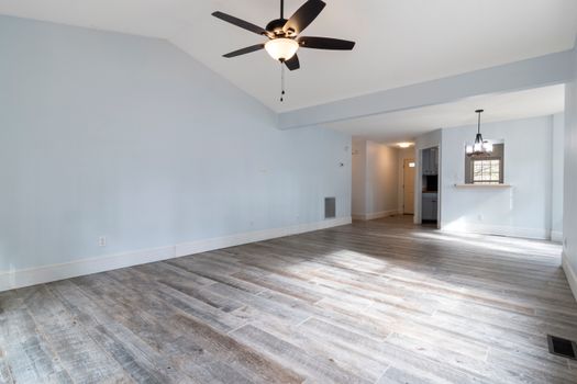 Bright and spacious empty living room with ceiling fan and wooden floor.