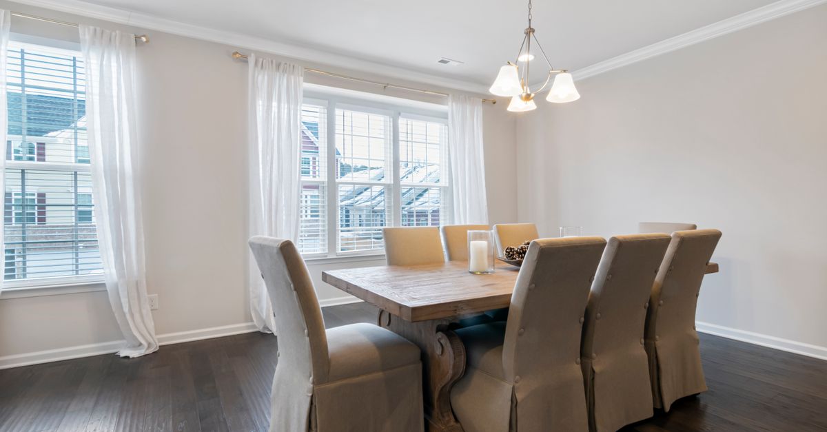 A bright dining room featuring a wooden table, upholstered chairs, and elegant lighting.