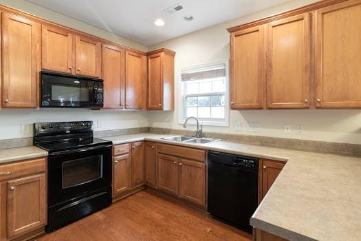 Interior of a modern kitchen featuring wooden cabinets, black appliances, and a large window.