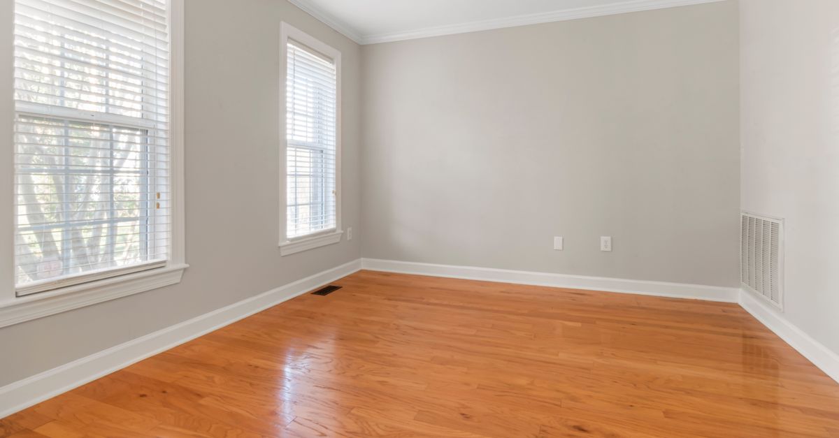 Spacious empty room with natural light, hardwood floors, and neutral walls.