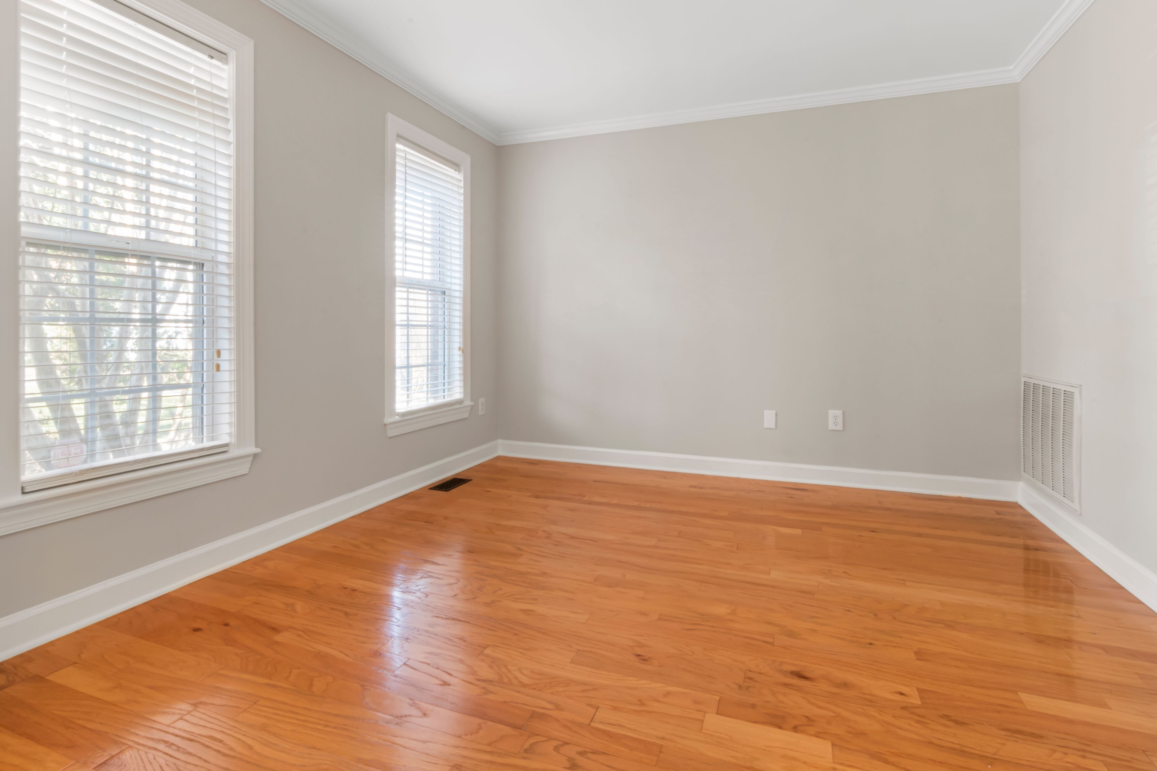 Un logement rendu habitable Grande pièce vide au parquet clair, largement éclairée par la lumière du jour