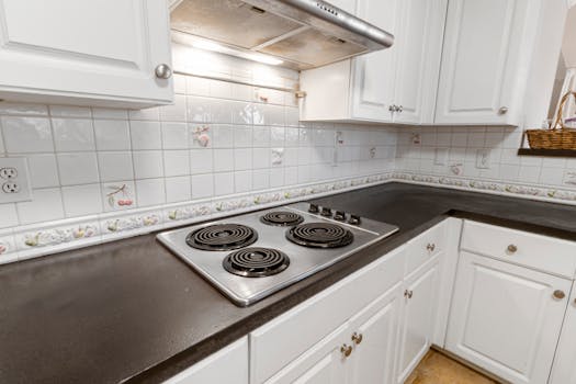 A clean and bright kitchen with white cabinetry, floral tile backsplash, and an electric stove top.