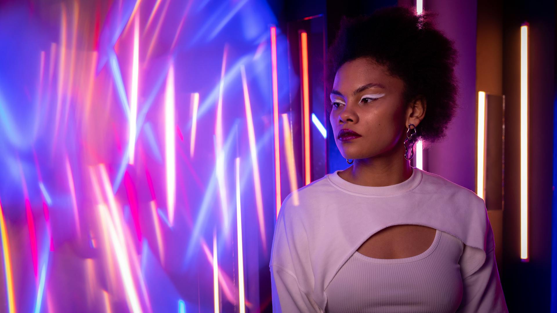 Woman in White Shirt with Eye Makeup Standing Near Neon Lights