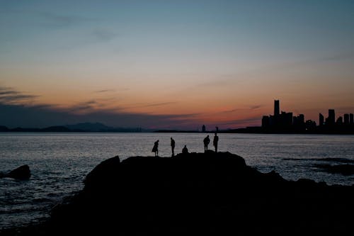Silhouette of People Standing on Rock Formation Near Body of Water during Sunset
