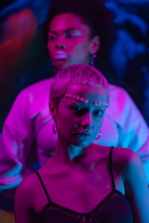 Free Two stylish young adults in a neon-lit setting showcasing modern fashion and artful makeup. Stock Photo