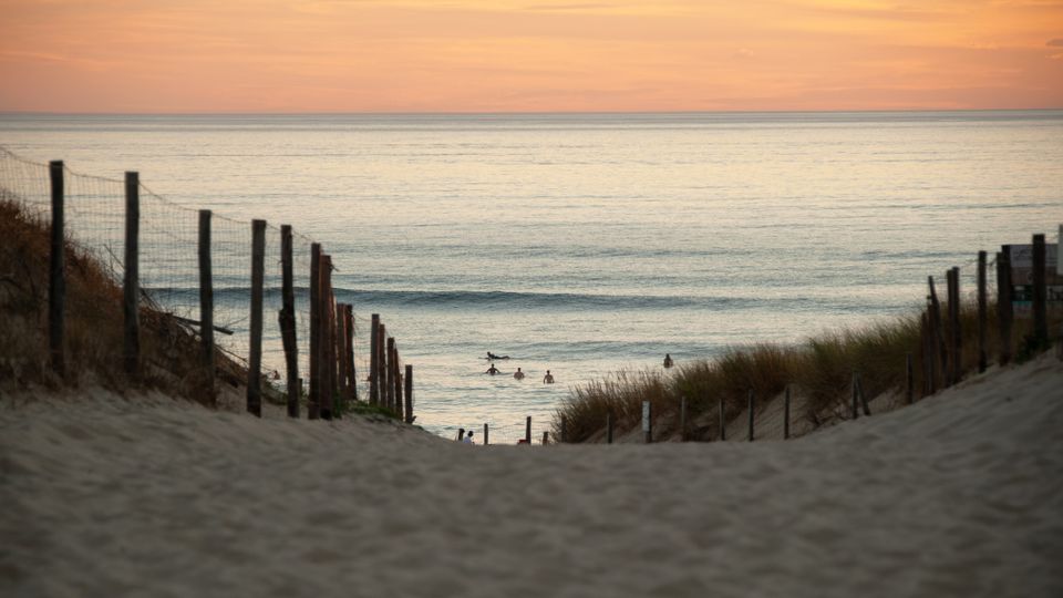 Serene beach scene at Seignosse with surfers during a radiant sunset.
