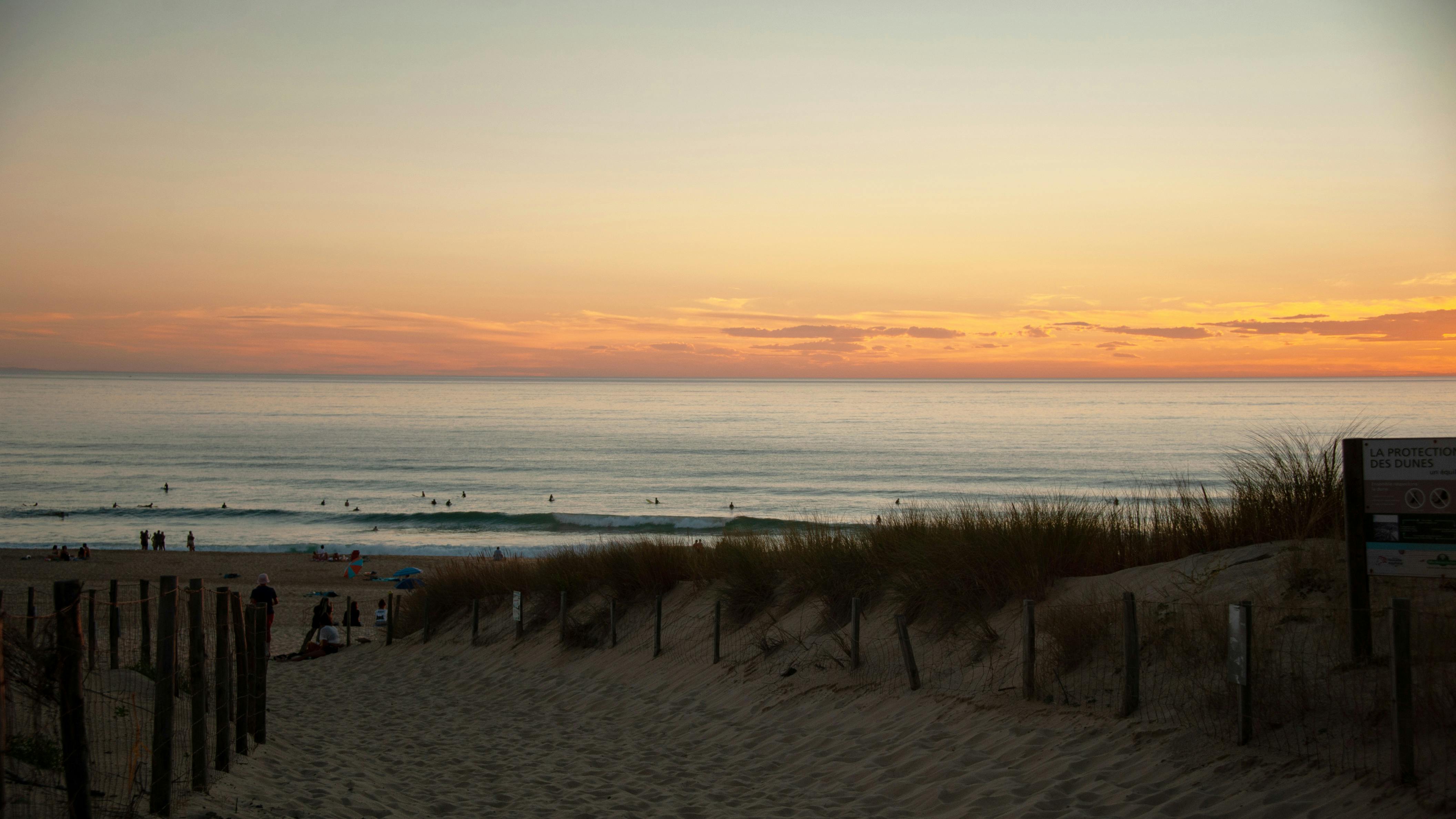 Hermoso atardecer sobre la Playa de Seignosse con surfistas disfrutando de las olas y vistas impresionantes del horizonte.