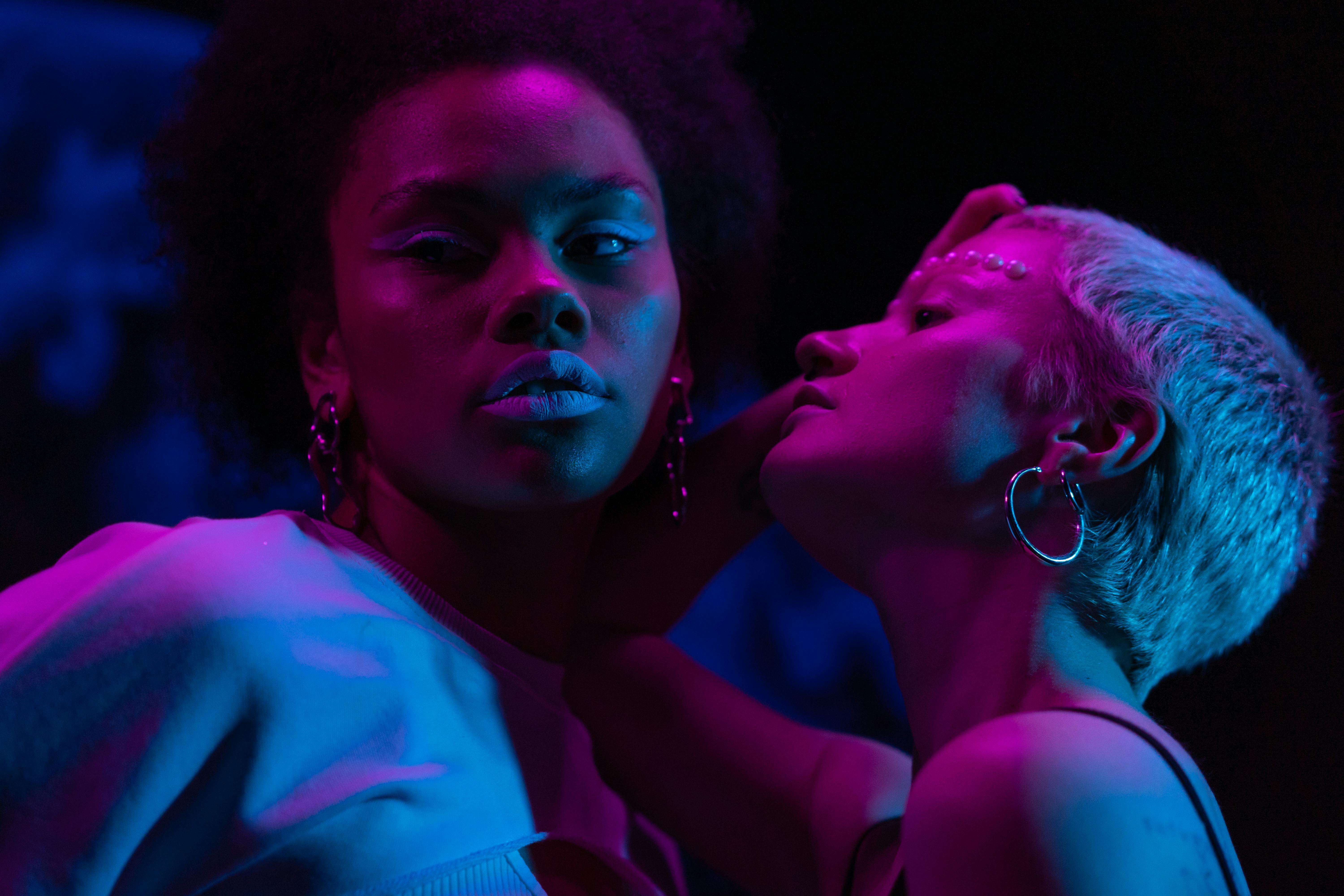 Close-up portrait of two stylish women in vibrant lighting creates a dramatic and artistic effect.