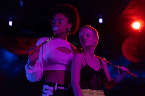 Stylish young women with bold makeup in neon-lit nightclub setting.