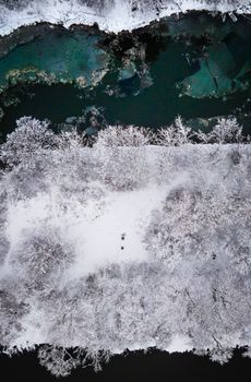 Stunning aerial perspective of a snow-covered forest next to a partially frozen river in winter.