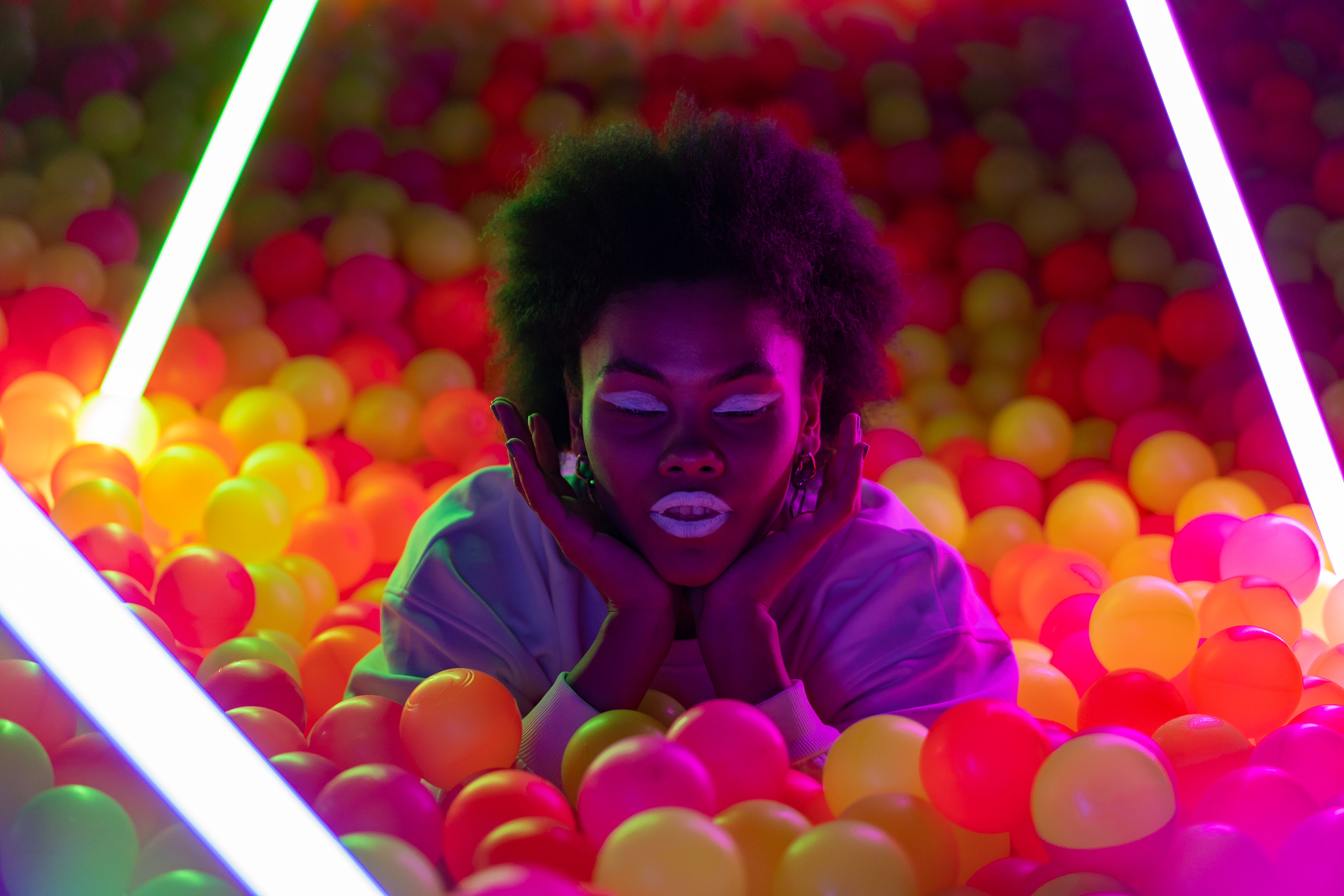 Artistic neon-lit portrait of a woman in a colorful ball pit with a futuristic feel.