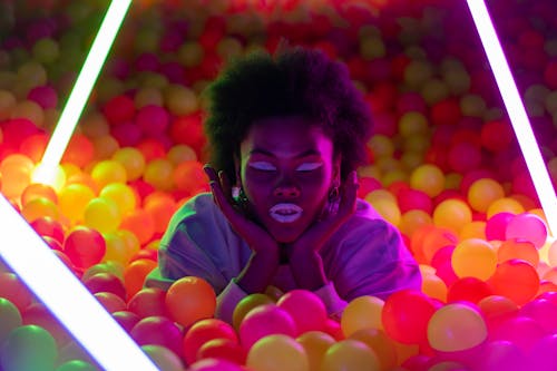 Artistic neon-lit portrait of a woman in a colorful ball pit with a futuristic feel.