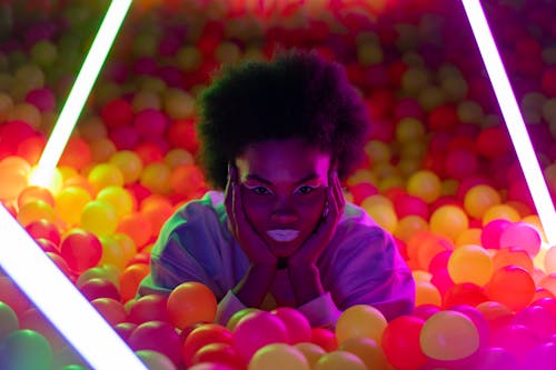 Bold portrait of woman with neon lighting in colorful ball pit. Futuristic and vibrant atmosphere.