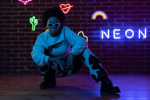 A Fashionable Woman Posing at the Camera Near the Brick Wall with Neon Sign